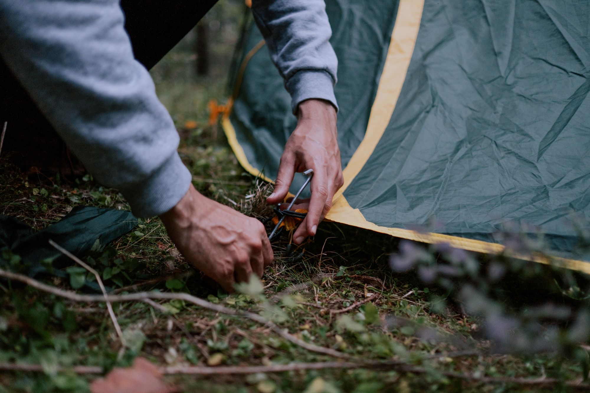 A camper securing a tent peg at a forested campsite